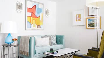 A modern living room with a teal sofa, a coffee table, a bar stool, and a green armchair.