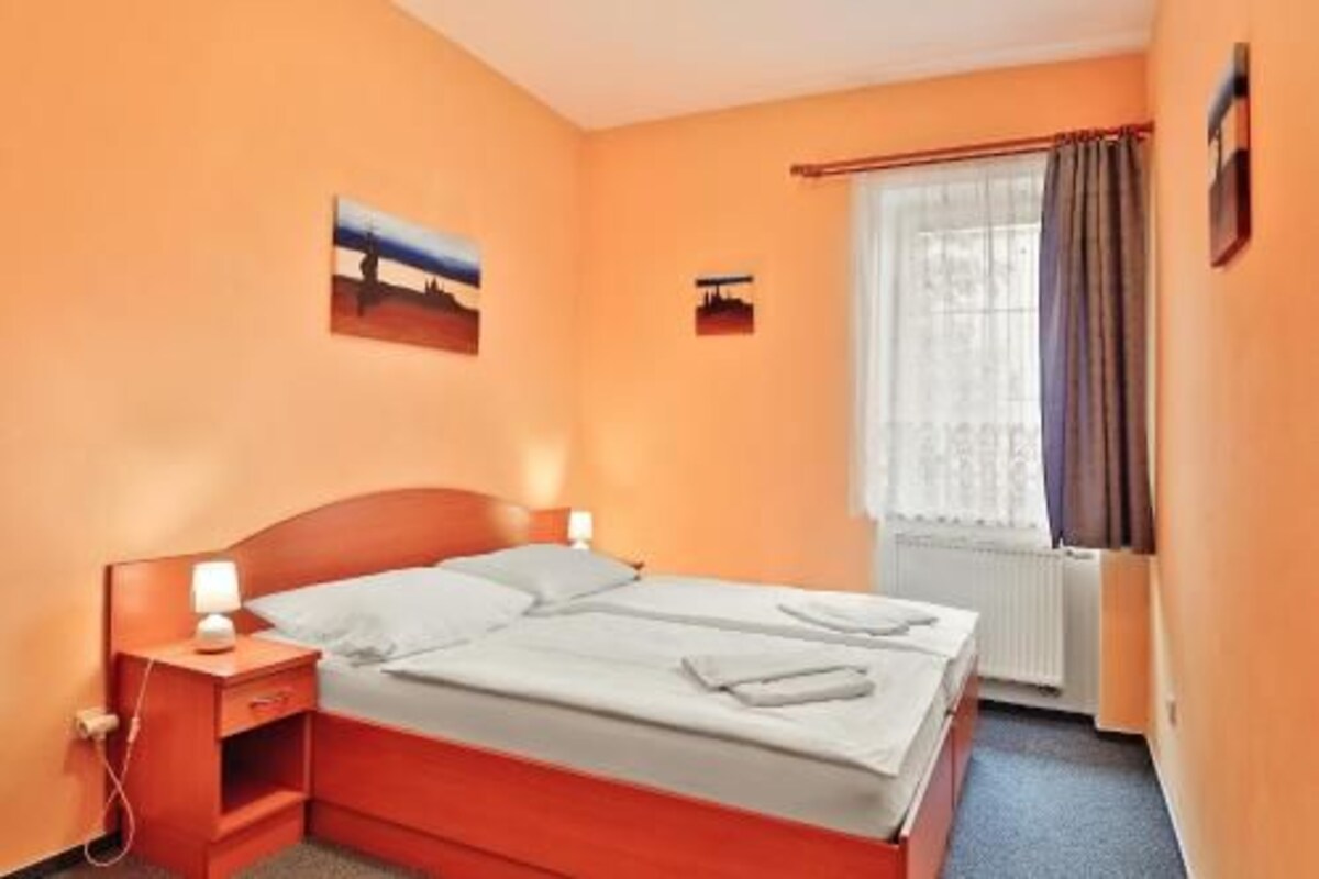 A hotel room with a wooden bed, a nightstand with a lamp, a window with curtains, and a painting on the wall.