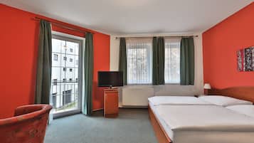 Habitación de hotel con una cama grande, televisor, ventana con cortinas y vista a un edificio.