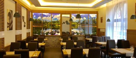 A restaurant with a view of a lake through large windows, wooden paneling on the walls, and pendant lighting.
