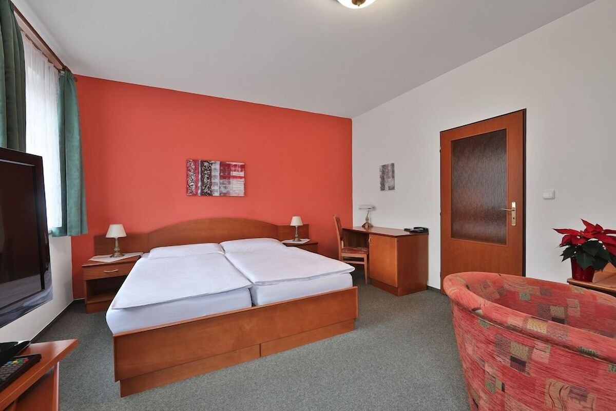 A hotel room with a bed, a desk, a chair, a TV, and a door.