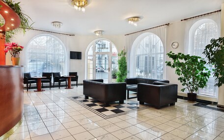 A spacious lobby with large arched windows, black leather sofas, and a checkered floor.