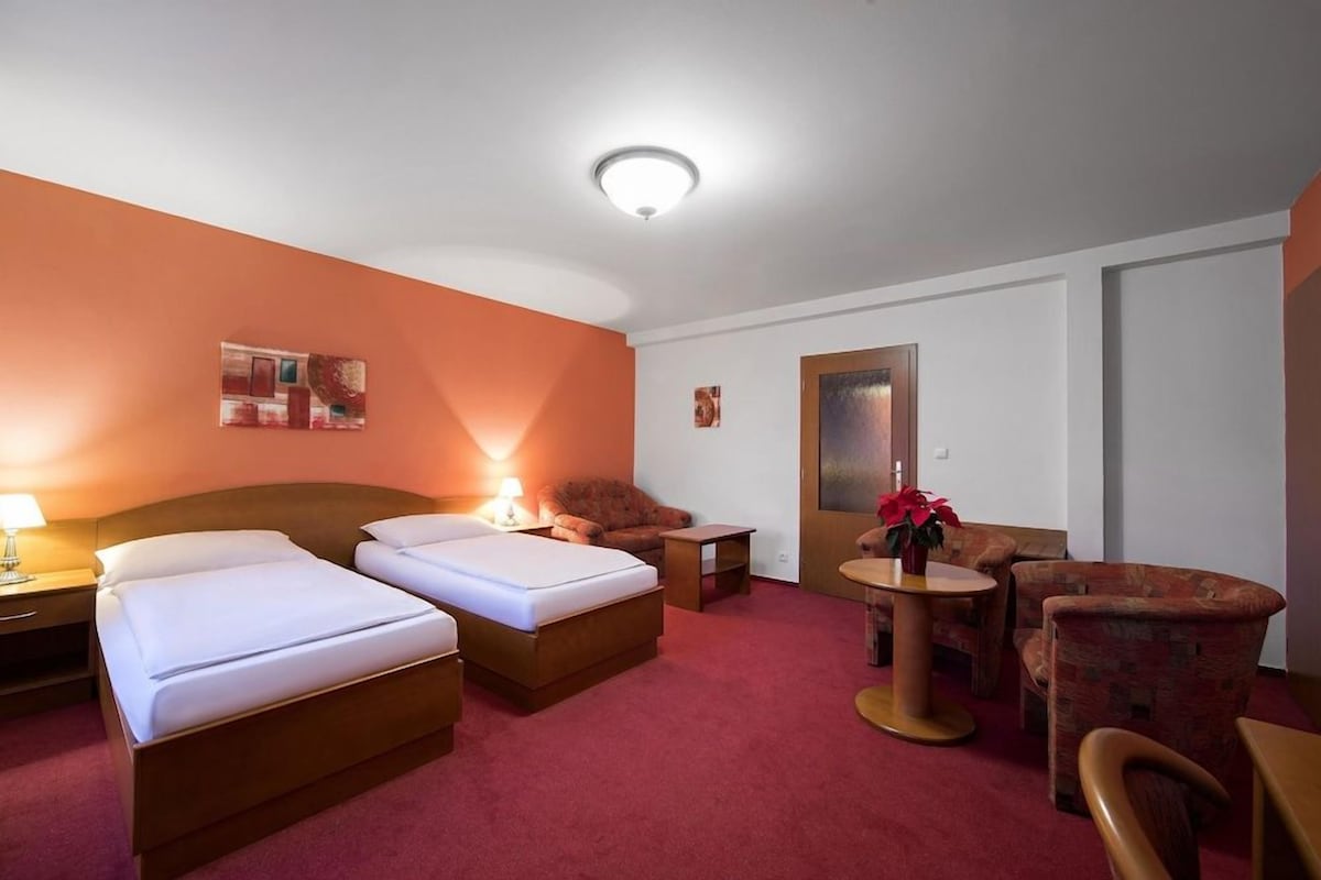 A hotel room with two beds, a sofa, a small table with a vase, and a mirror on the wall.