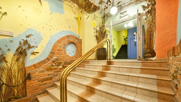Una escalera con un muro de ladrillo y un mural, que conduce a una habitación con un reloj y un letrero que dice "Hotel".