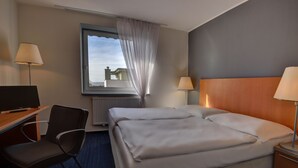 Habitación de hotel con cama, escritorio con silla, televisor y dos lámparas.
