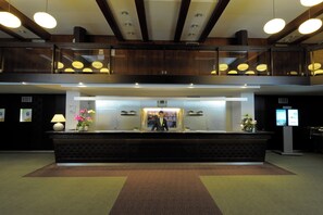 A hotel reception area with a reception desk, a digital display, and a view of the cityscape through the windows. - Olsanka (Prague)