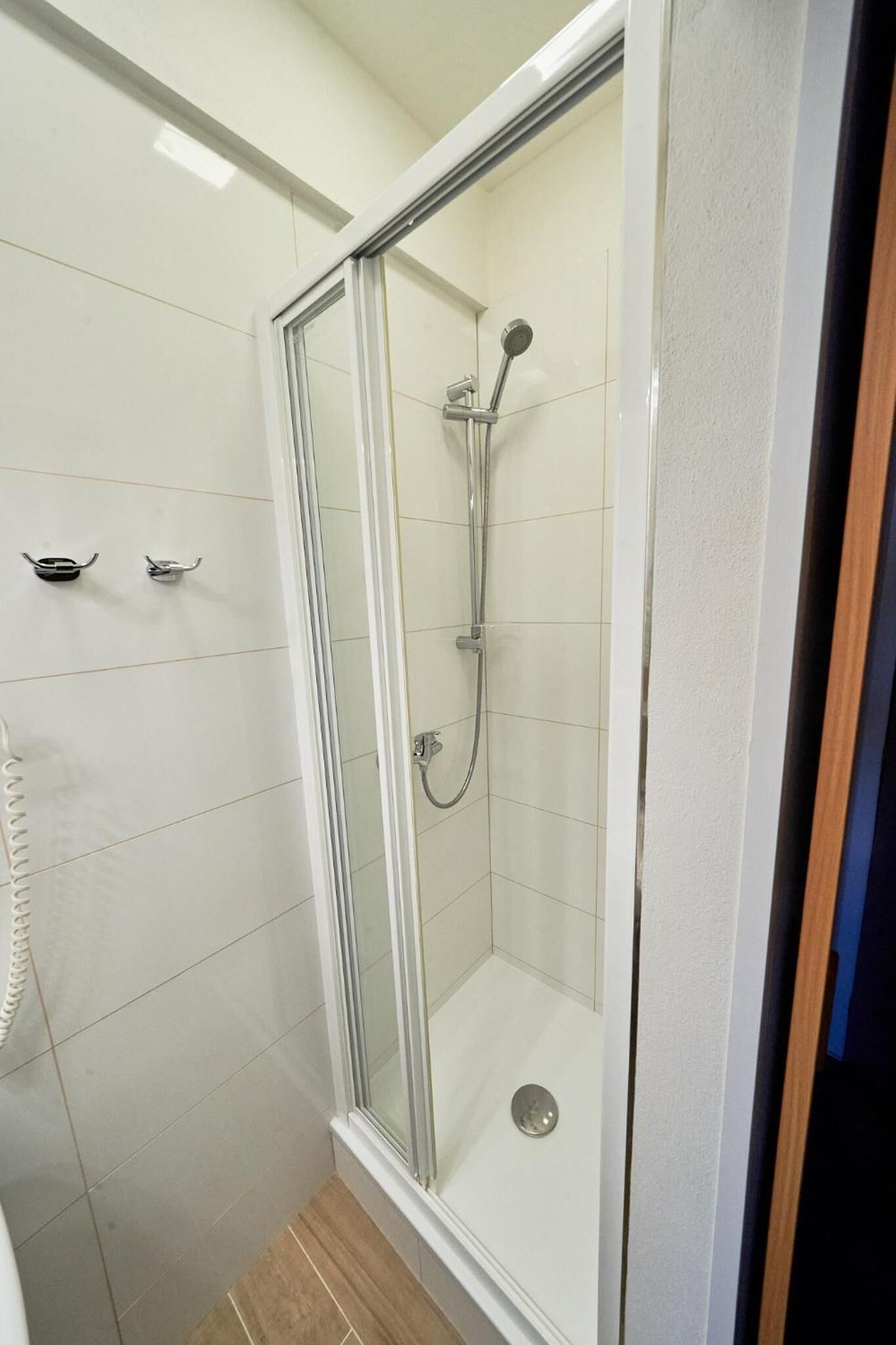 Una ducha envuelta en vidrio con un cabezal de ducha de mano y un grifo instalado en la pared.