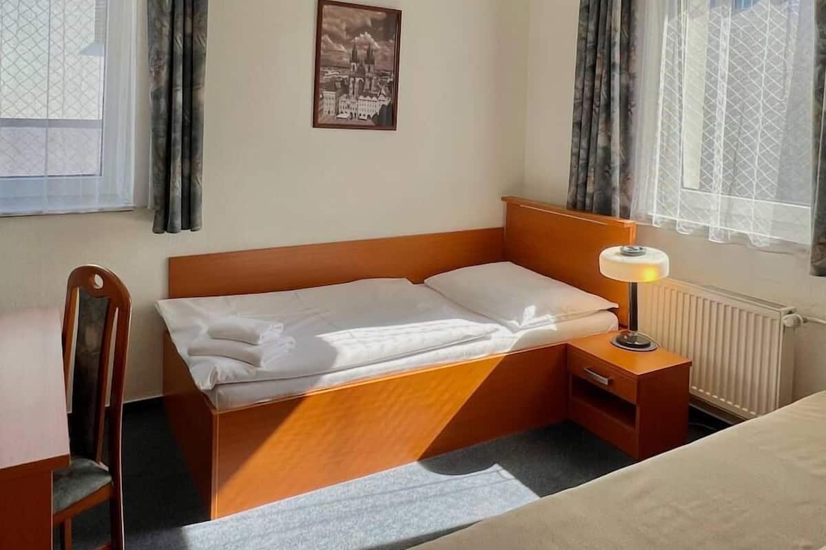 Quarto de hotel com cama, escrivaninha, cadeira, luminária e janela com cortinas.