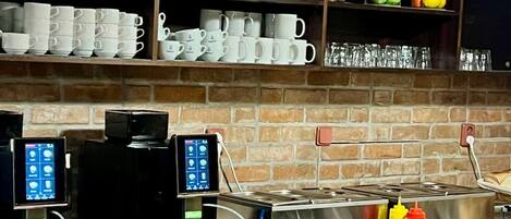 Una zona de cafè amb diverses màquines de cafè, una varietat de tasses i dispensadors de condiments.