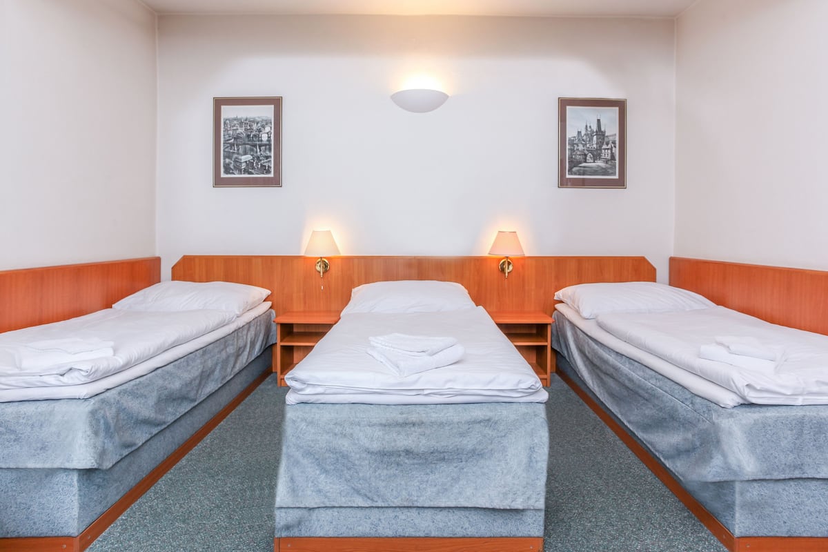 Quarto de hotel com duas camas de solteiro, cabeceira de madeira, carpete cinza e duas luminárias fixadas na parede.
