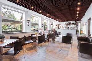 Uma área de refeições moderna, com grandes janelas, um bar e disposição de assentos.