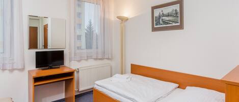 A hotel room with a wooden bed, a desk with a TV, a radiator, and a window with curtains.