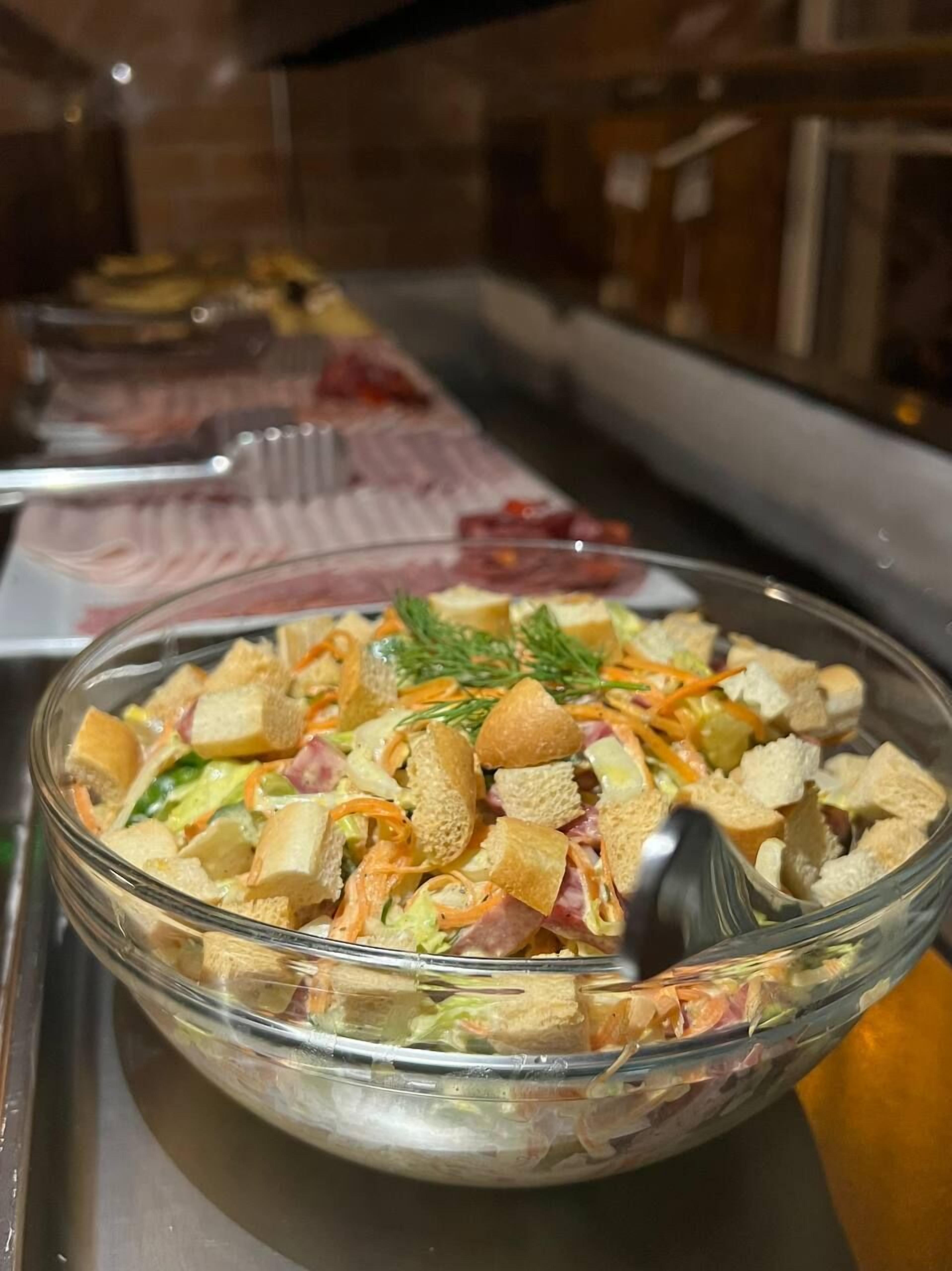 Un bol de vidrio con ensalada, crutones y vegetales sobre una bandeja.