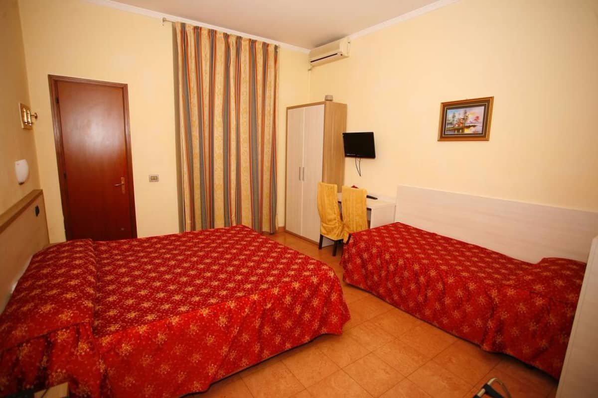A hotel room with two single beds, a wardrobe, a desk with a chair, a television, and a curtain.