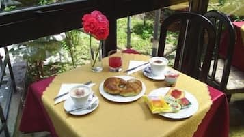 A table set with a meal, including croissants, a cup of coffee, and a glass of juice, on a veranda with a view of greenery.