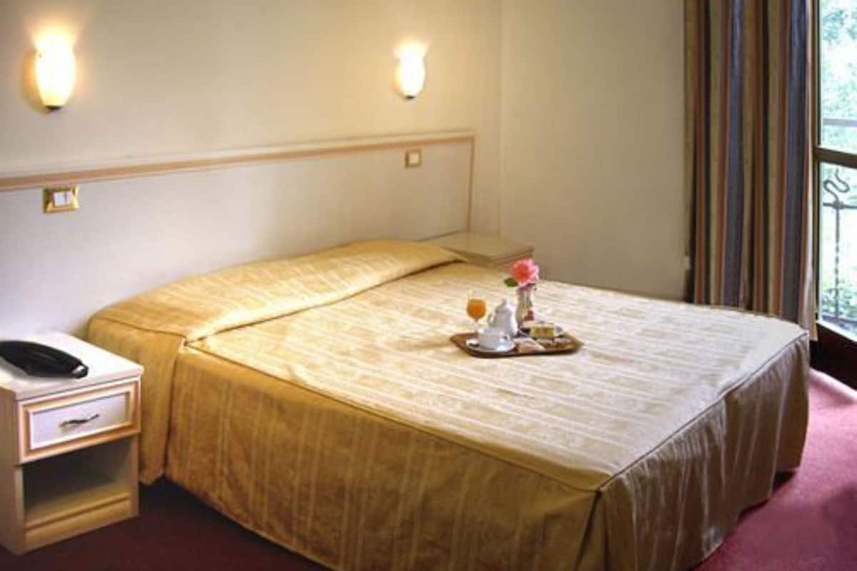 A neatly made bed with a tray of breakfast items, a bedside table with a phone, and a window with curtains.