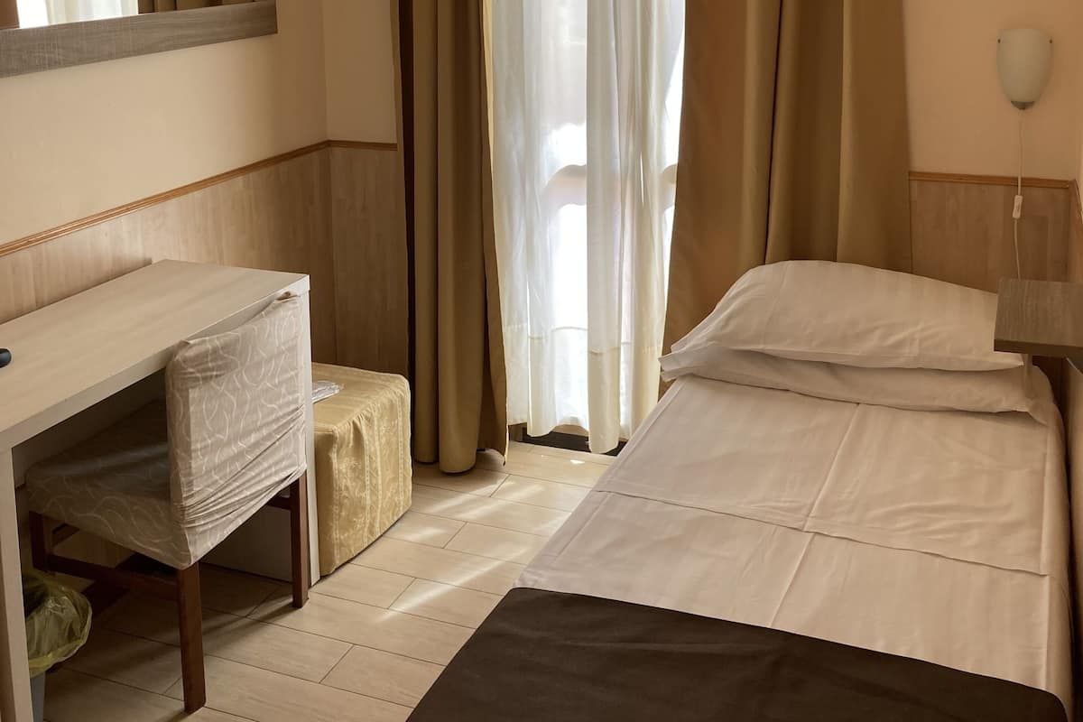 A hotel room with a bed, a desk, a chair, a mirror, and a window with curtains.