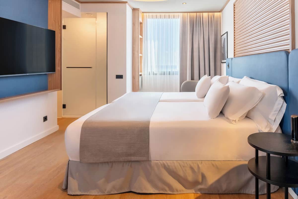 Habitación de hotel moderna con una cama grande, un televisor de pantalla plana, una mesita y una ventana con cortinas.