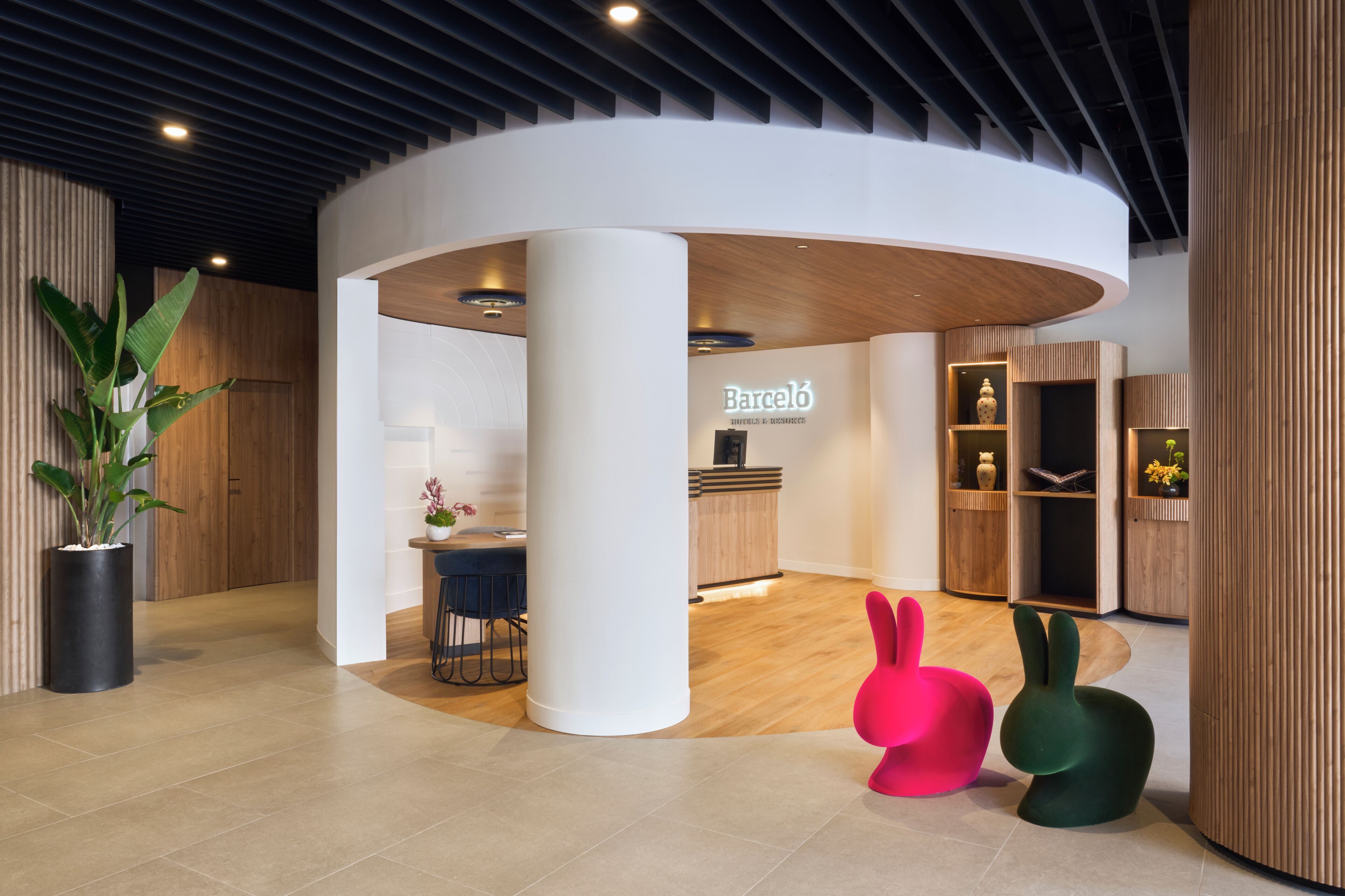 Un interior moderno con un mostrador de recepción, una planta en maceta y dos esculturas de conejos de colores.