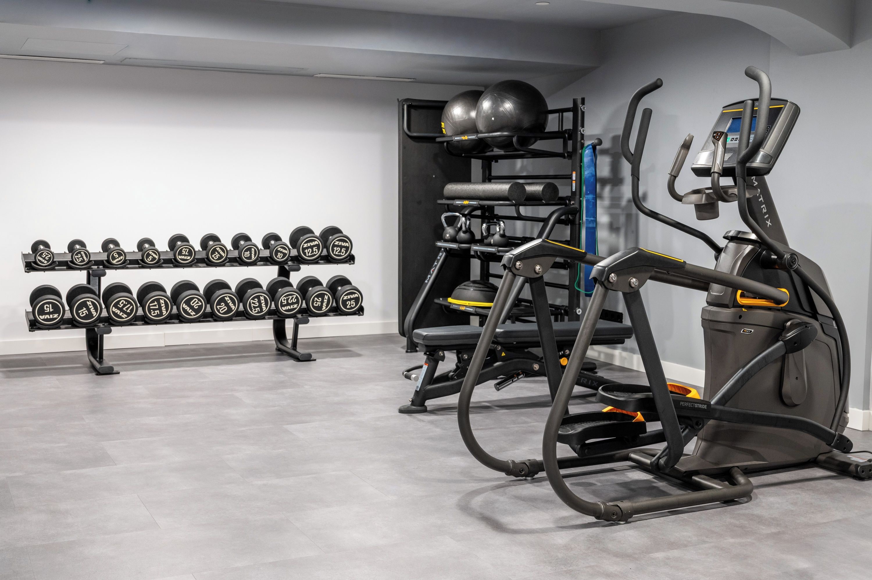 Ein Fitnessstudio mit Trainingsgeräten, darunter Hanteln, Kettlebells und ein Laufband.