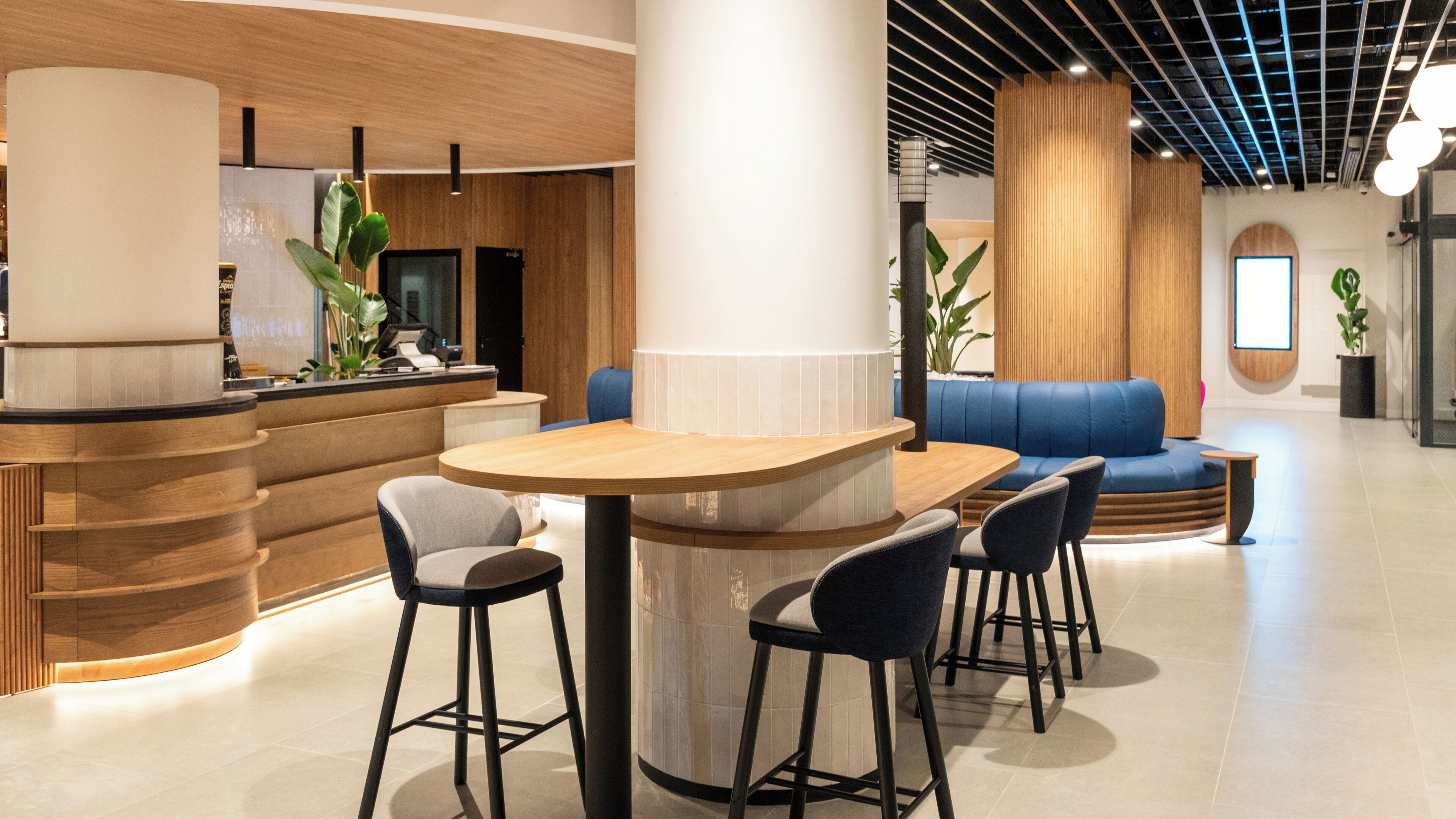 A modern interior with a wooden reception desk, bar stools, a blue sofa, and a large pillar.