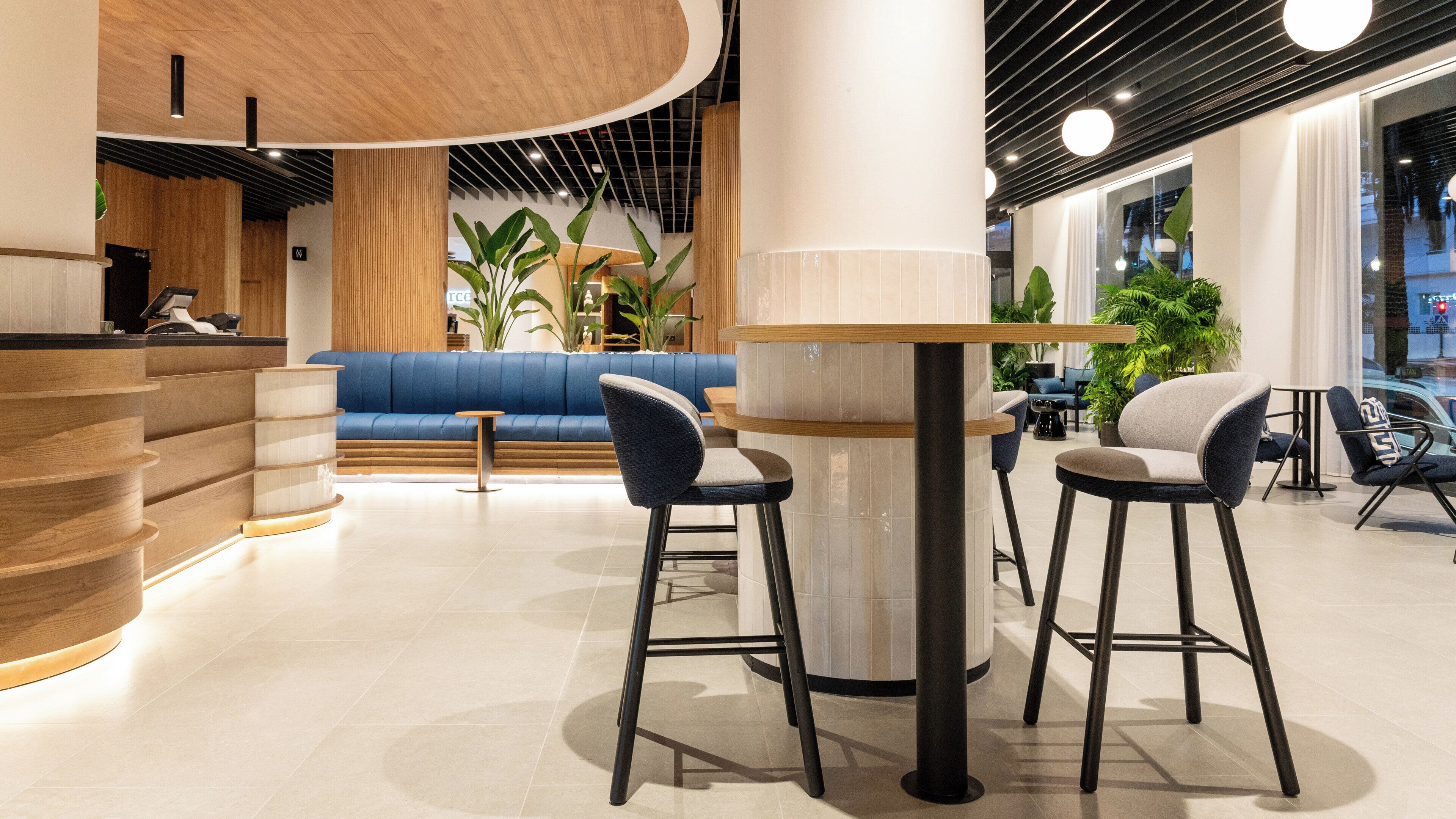 A modern interior with a reception desk, blue seating area, and bar stools.