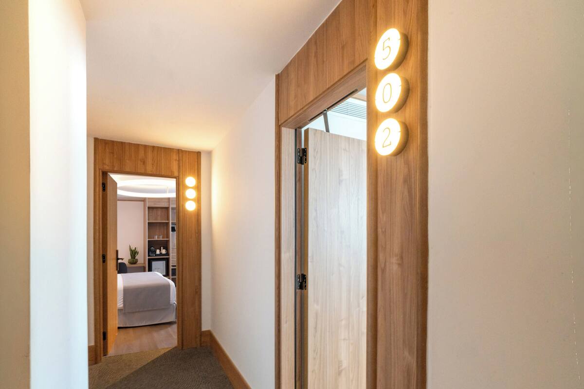 Un pasillo con piso alfombrado, paredes de madera y una puerta con números iluminados.