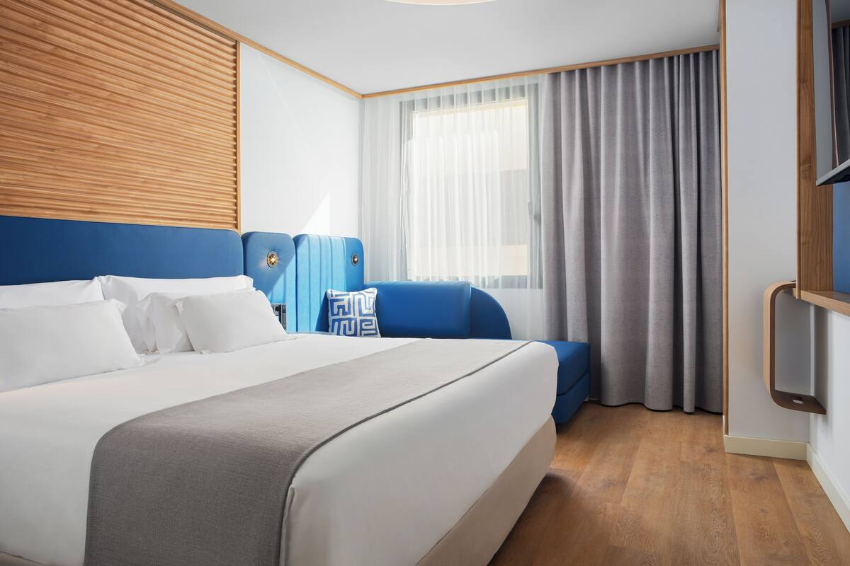 Una habitación de hotel moderna con una cama grande, un sofá azul y una ventana con cortinas.