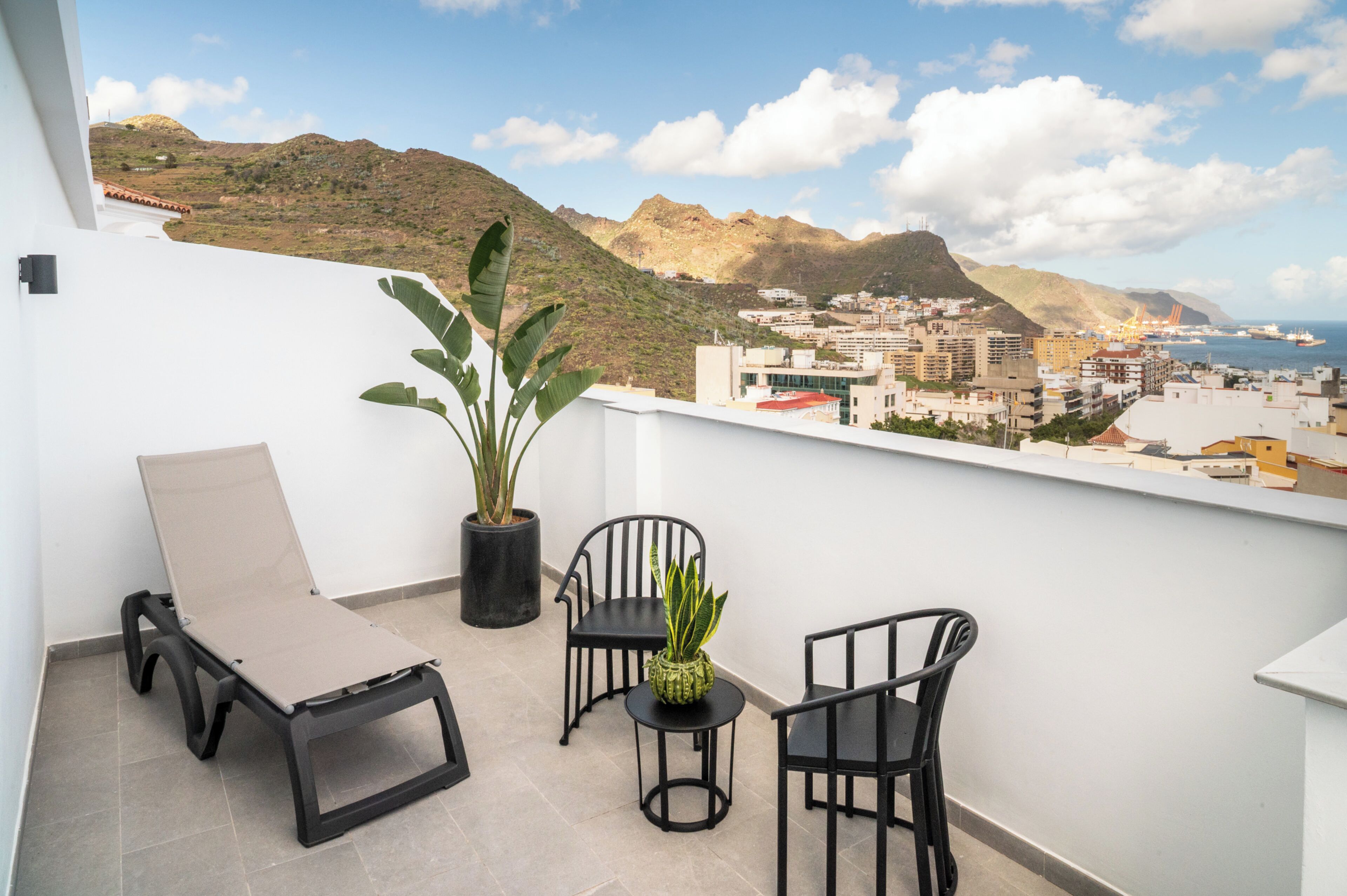 Un balcon avec un fauteuil de relaxation, deux chaises, une petite table et une plante en pot.