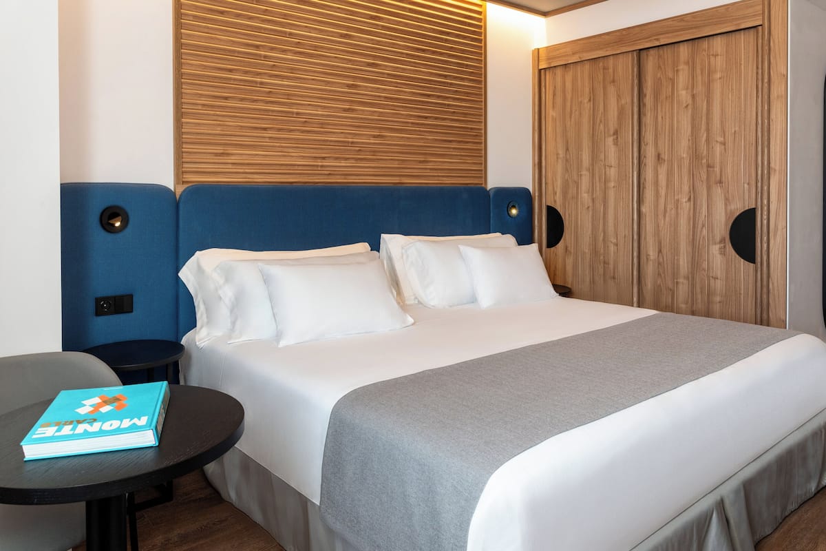 Una habitación de hotel con una cama, una mesa redonda con un libro y un cabecero de madera.
