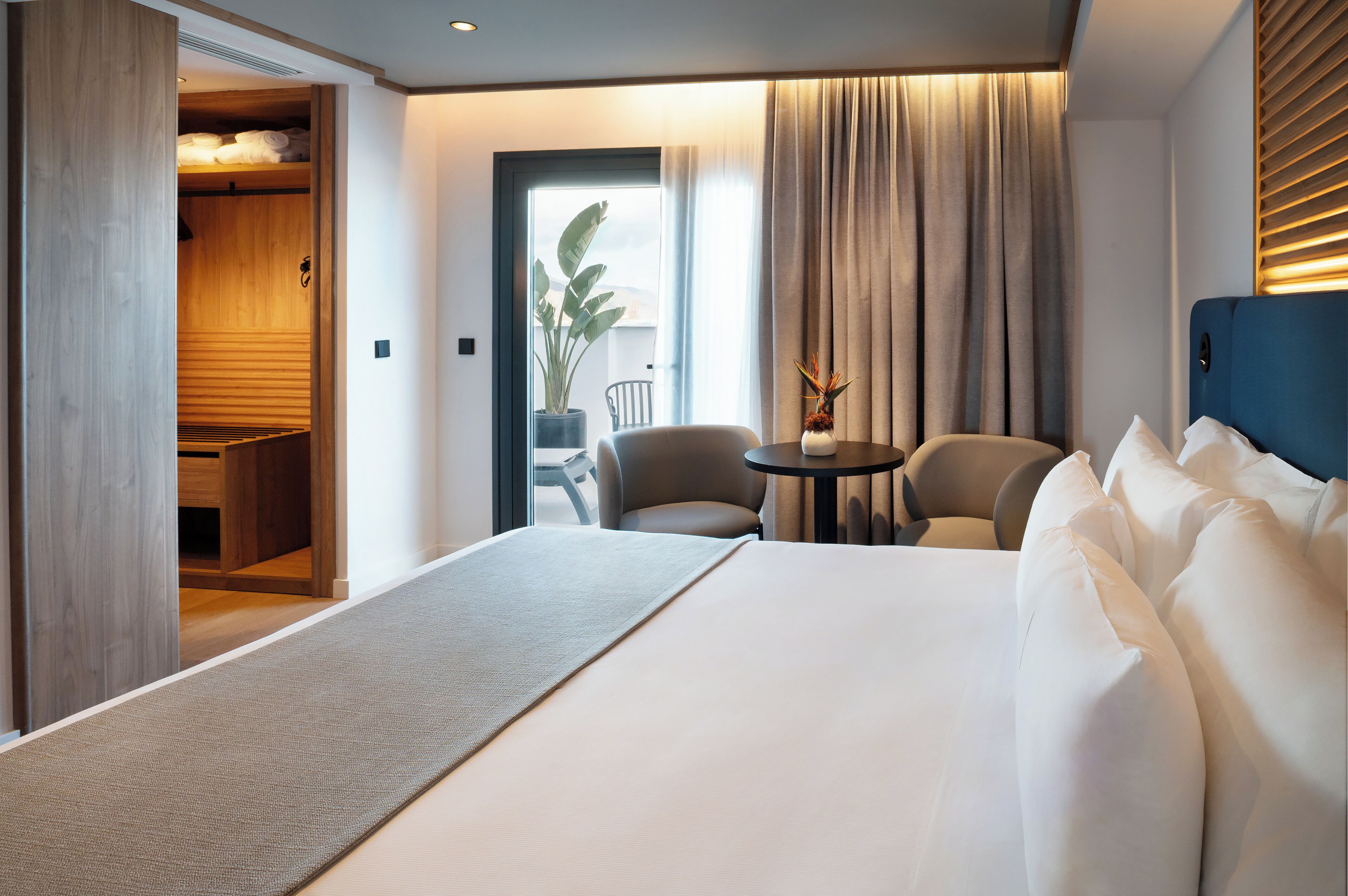 A hotel room with a large bed, a seating area with chairs, a small table, and a potted plant.