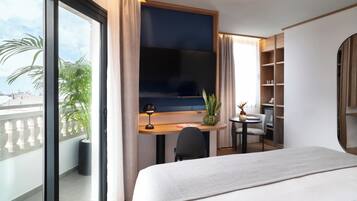 Habitación de hotel con cama, escritorio con televisor, una mesita, una silla, planta en maceta y vista a la ciudad.