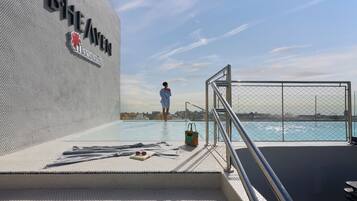 A poolside area with a person walking towards the water, a sign reading 'B1HEAVEN', and a view of the sea.
