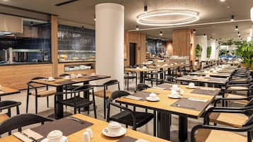 A modern restaurant with multiple dining tables and chairs, a kitchen area, and a decorative ceiling light.