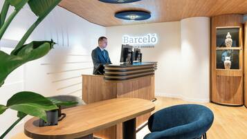 A modern reception desk with a man standing behind it, a wooden counter, and a wall-mounted sign that reads "Barceló RESORTS".