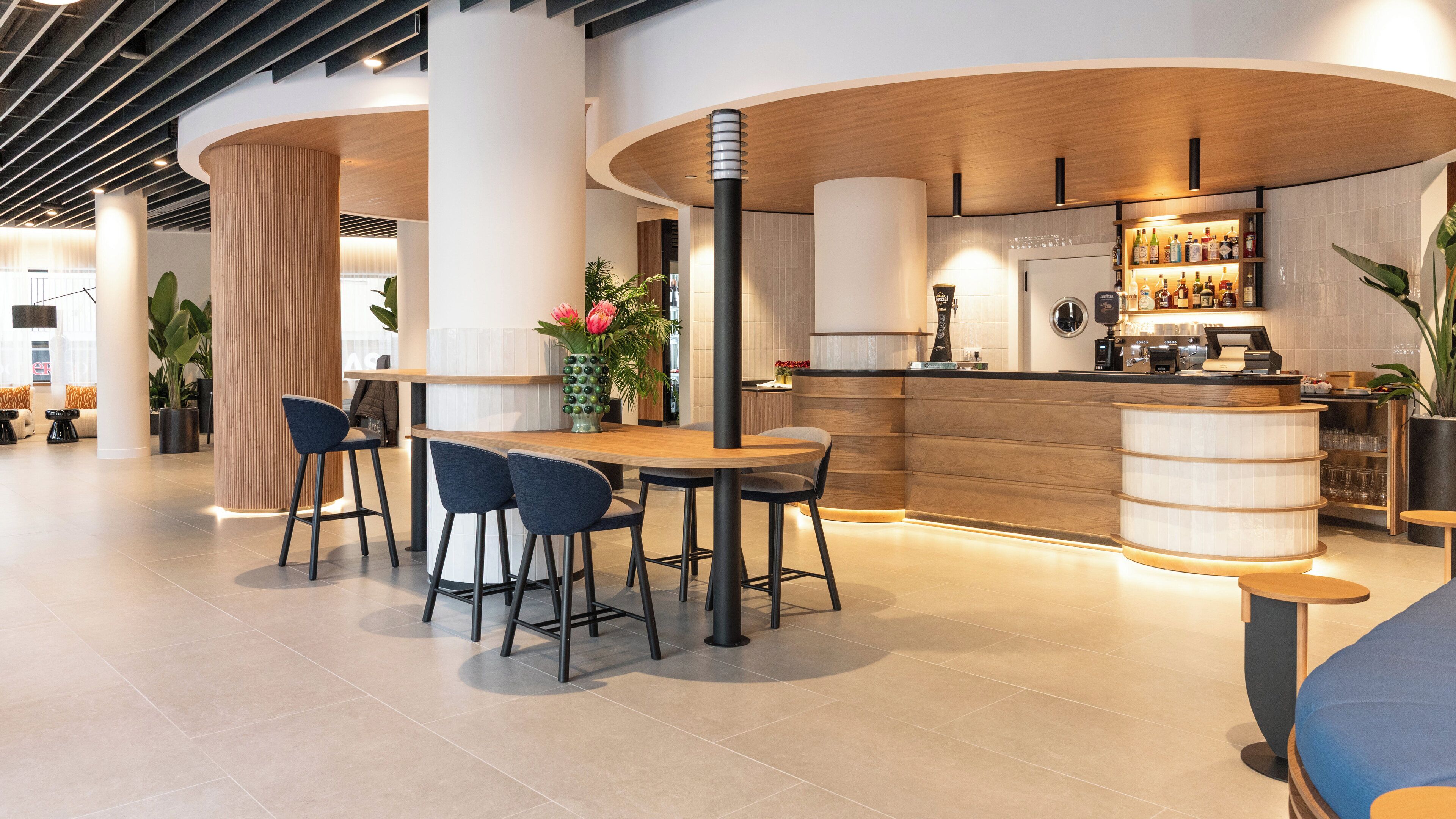 Un bar moderno con mostrador de madera, taburetes y una zona de estar con mesa y sillas.
