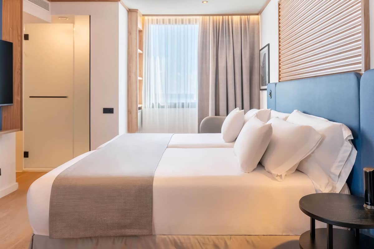 Un hotel moderno con una cama grande, un televisor, un escritorio y vistas a la ciudad desde la ventana.