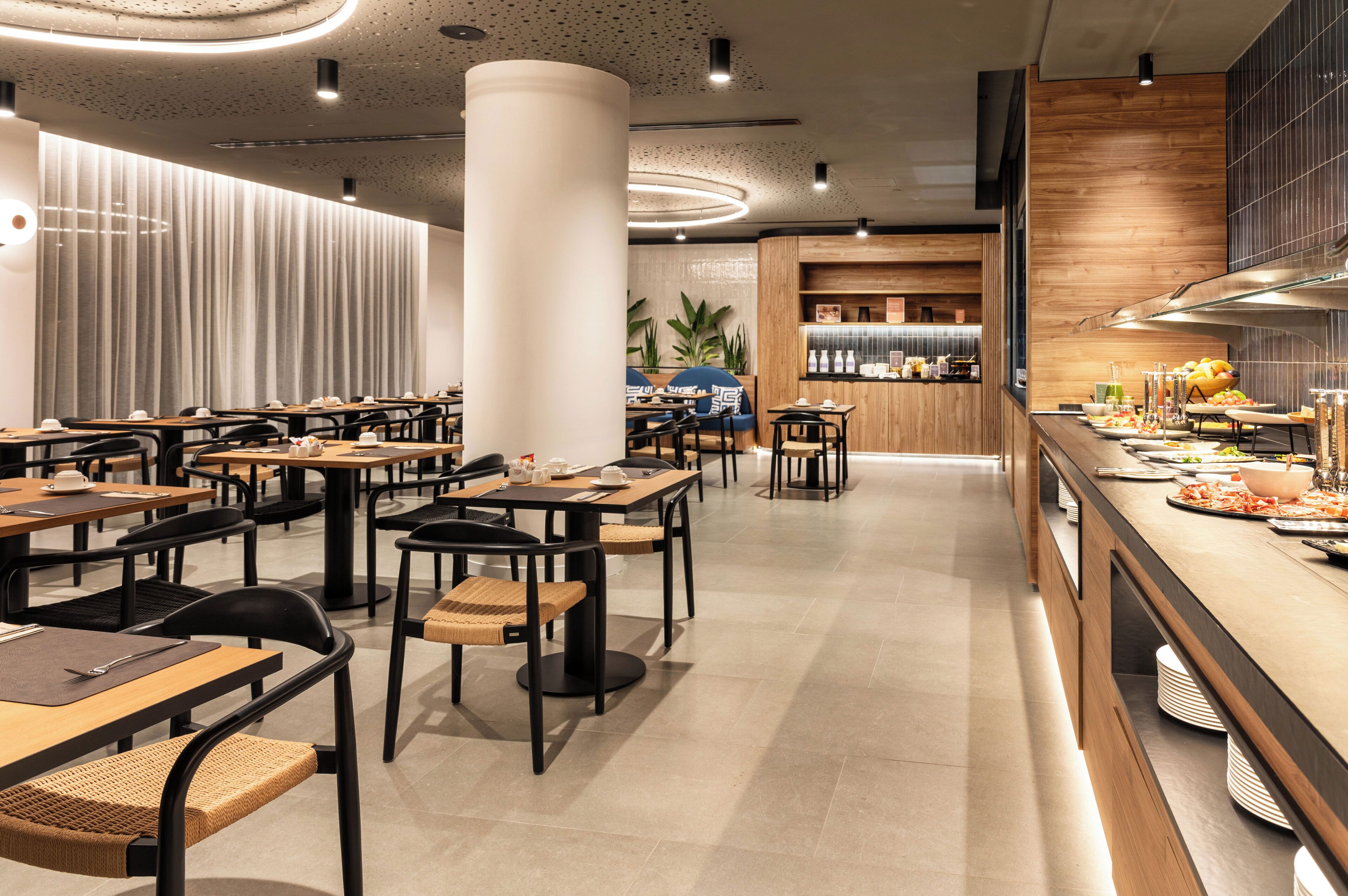 Un restaurant moderne doté de plusieurs tables et chaises, d’un comptoir où sont servis des plats et des boissons, et d’un espace cuisine.