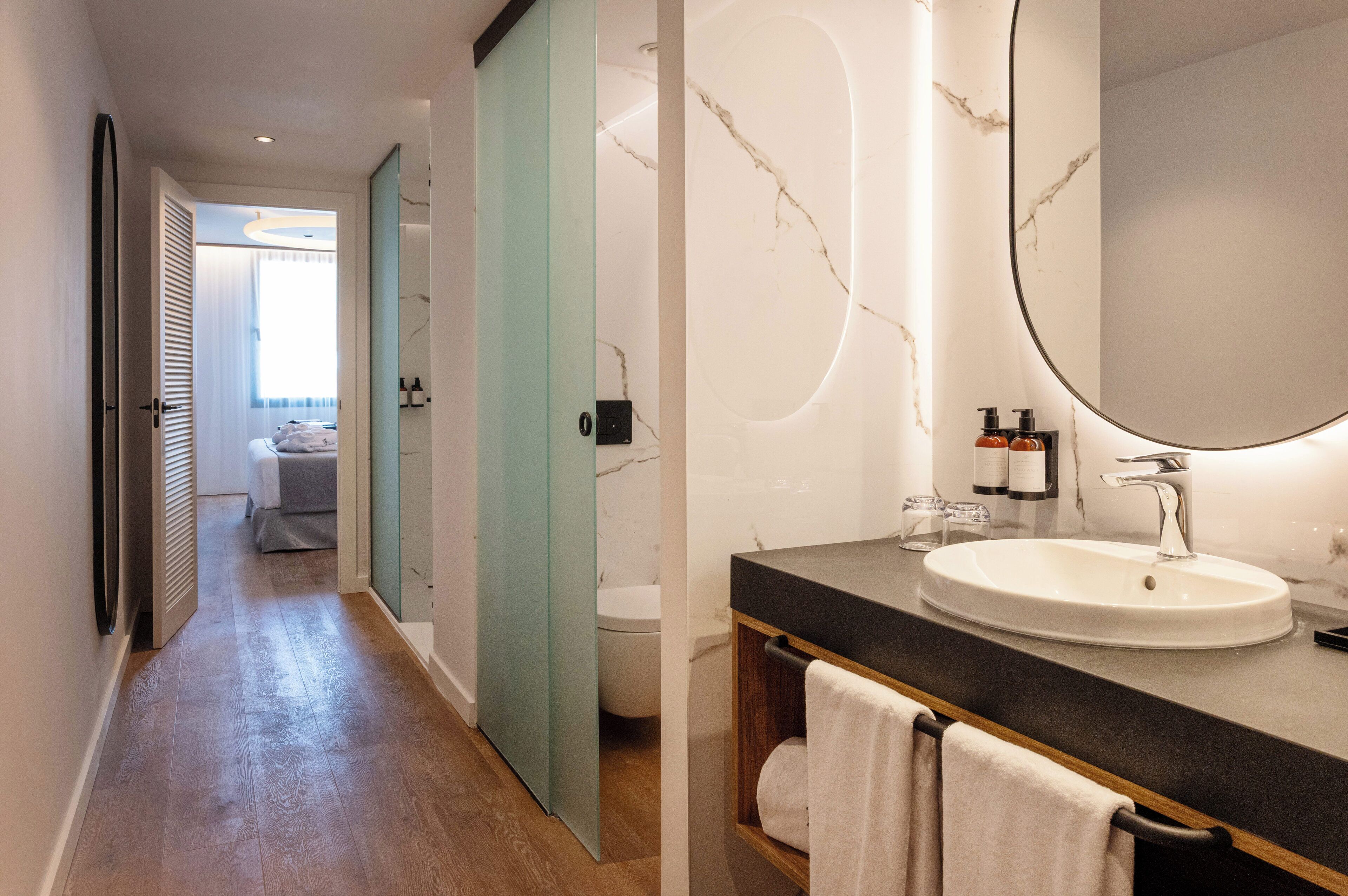 A modern bathroom with a marble wall, a round mirror, and a wooden vanity.