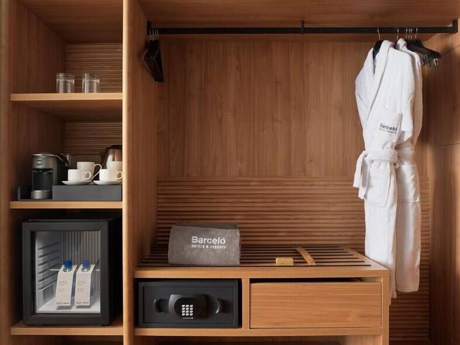 Un armario de madera con minibar, una bata colgada en la puerta y un minibar con cafetera y tazas.