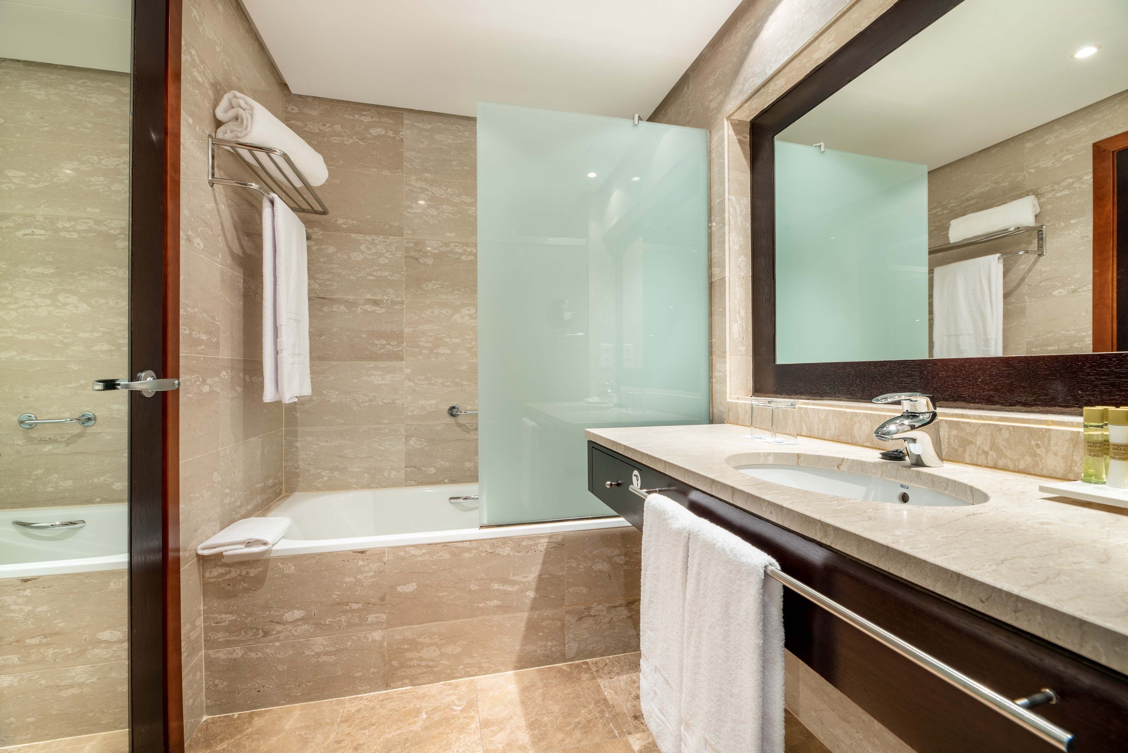 A modern bathroom with a glass shower enclosure, a bathtub, and a vanity with a sink and mirror.