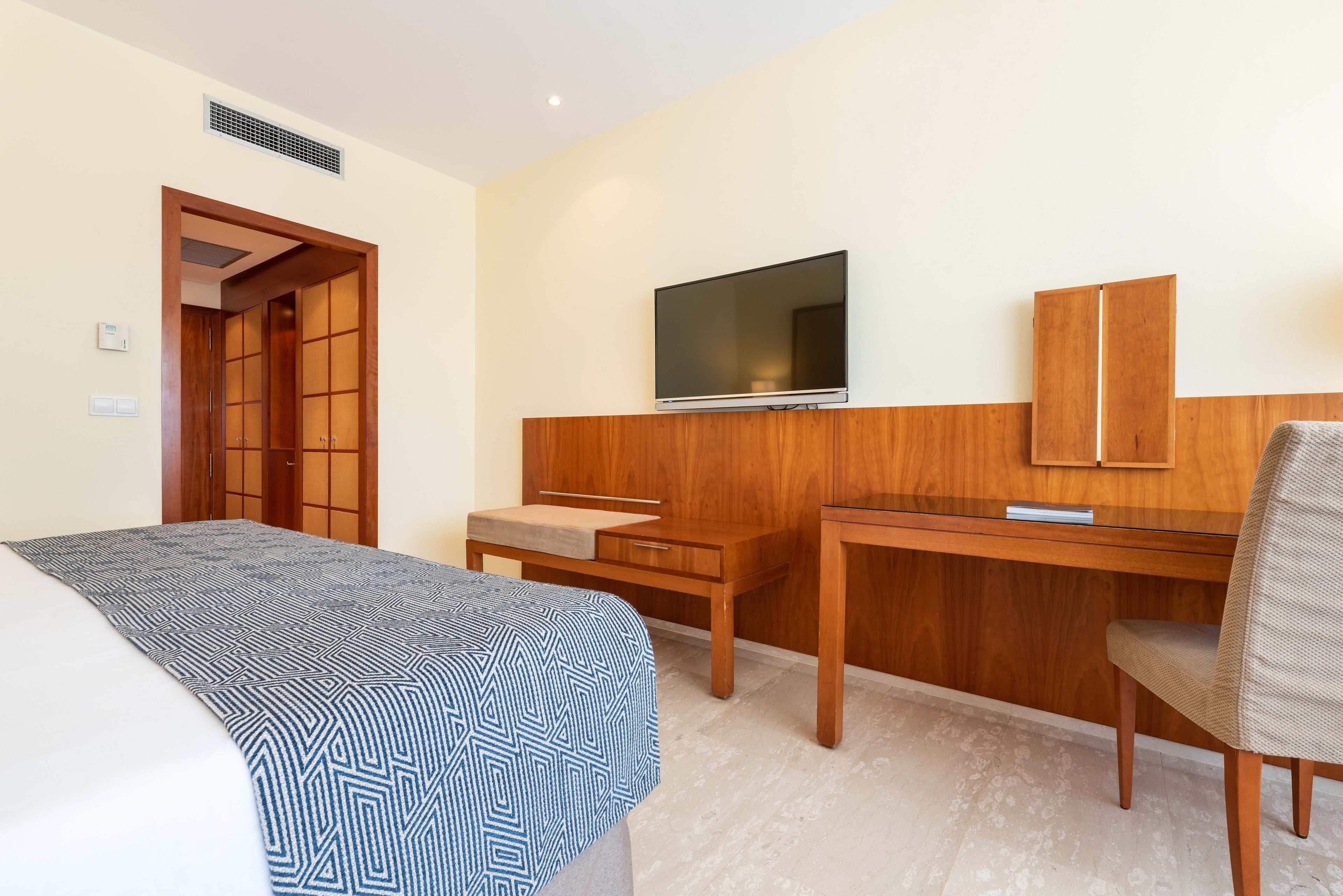 Habitación de hotel con cama, escritorio, silla, televisor y armario.