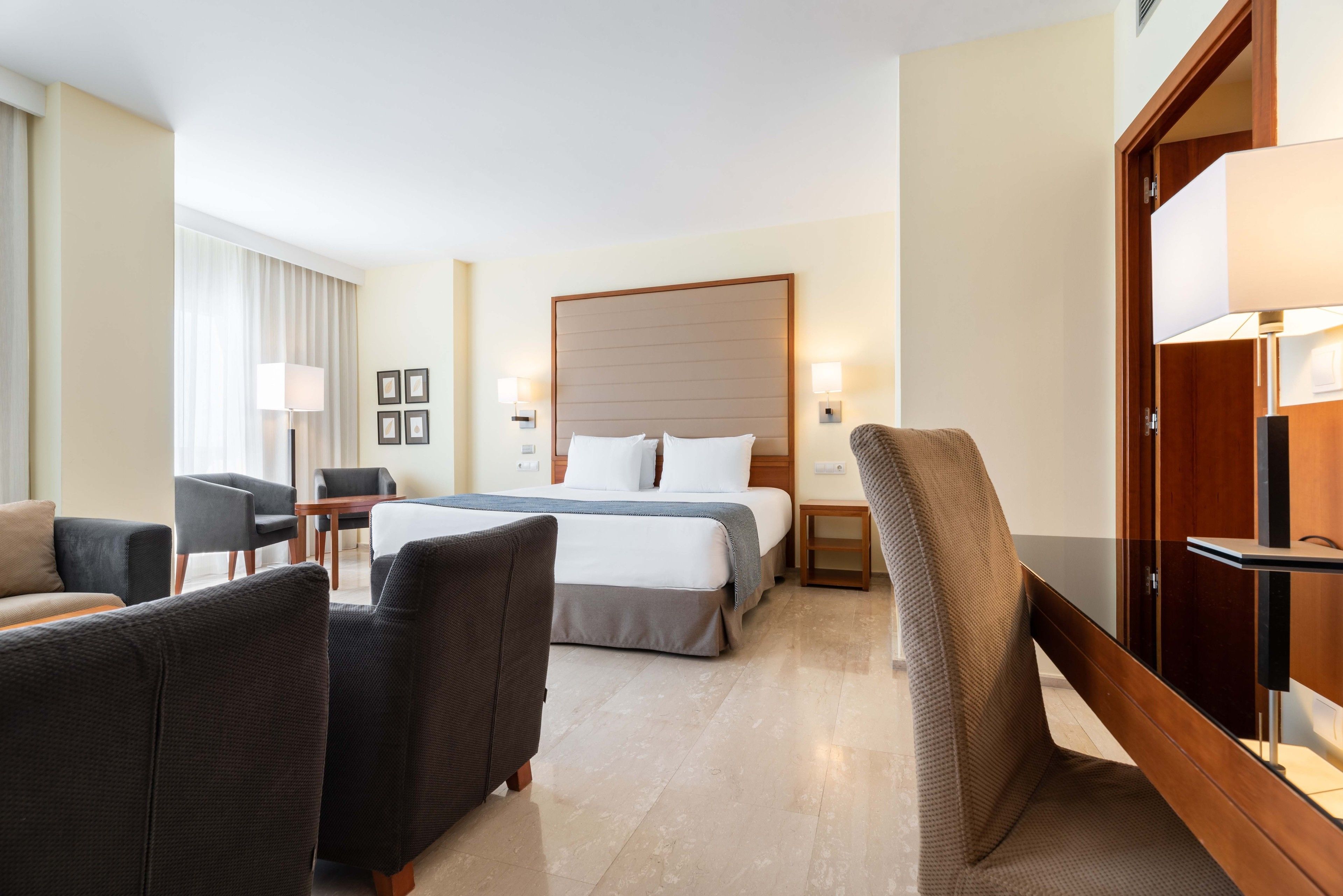 Una habitación de hotel con una cama, dos sillones, una mesita y un escritorio.