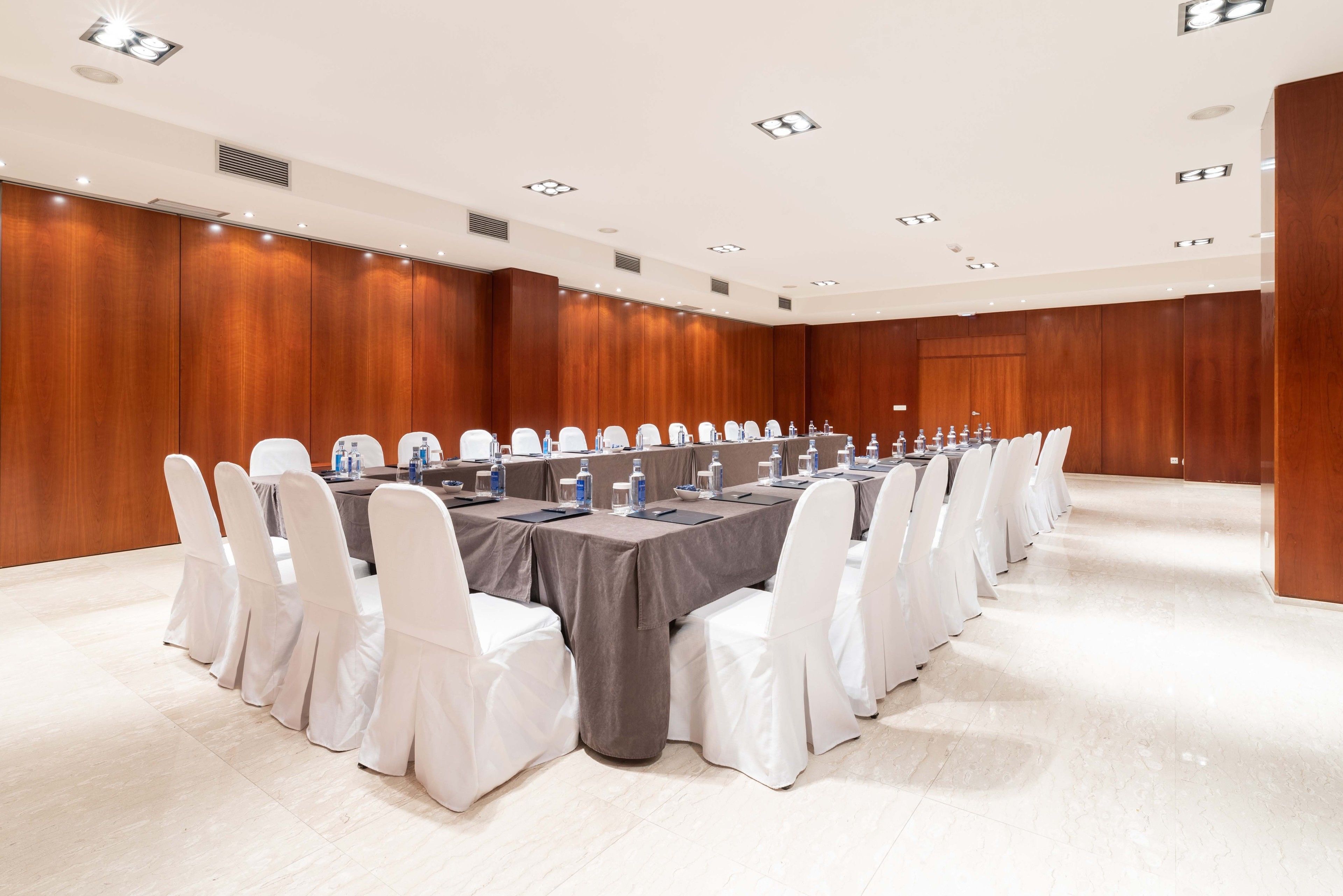 A conference room with a long table, white chairs, and a wooden panel wall.