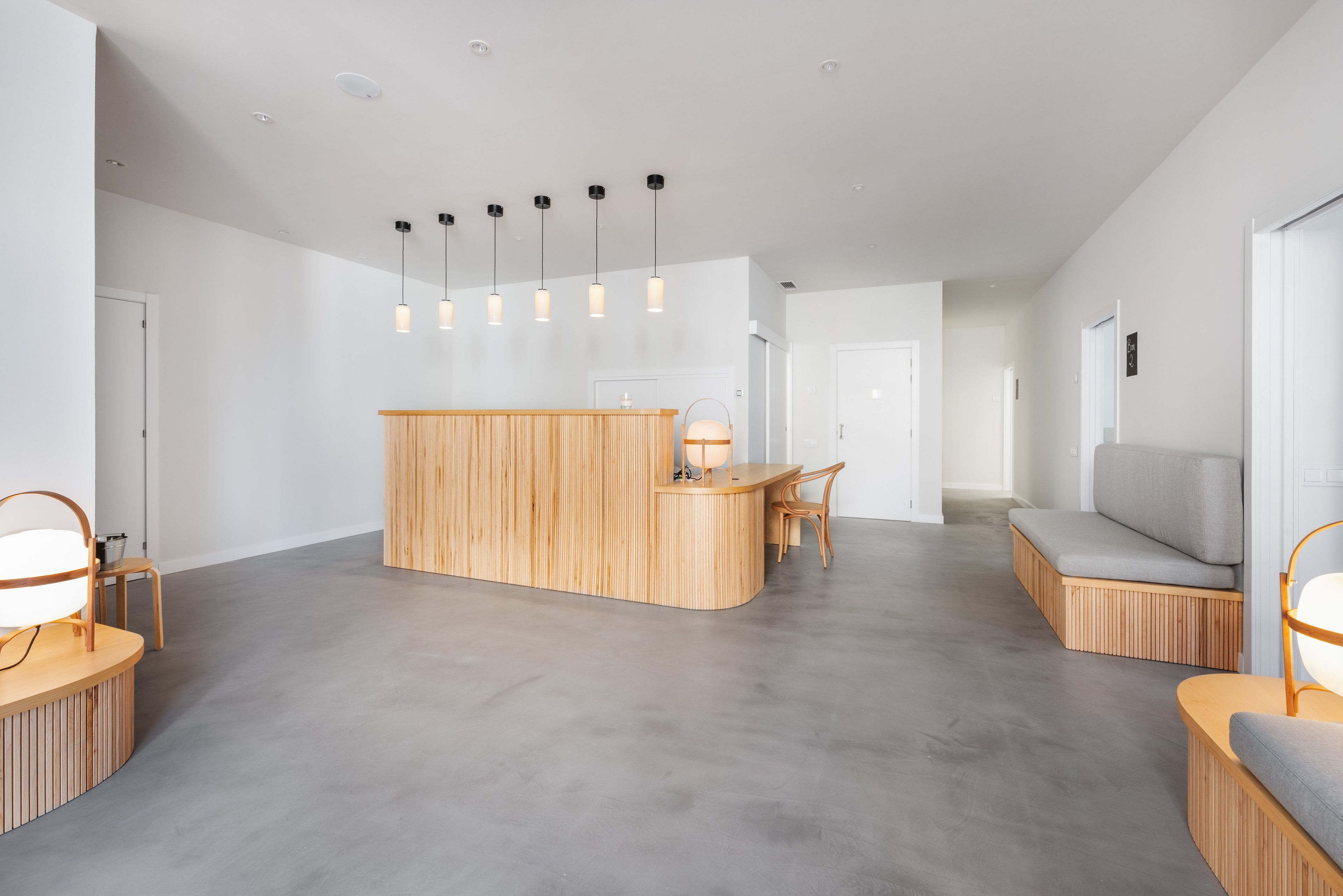 A modern reception area with a wooden counter, a seating area with a grey sofa, and pendant lighting.
