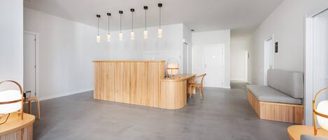 A modern reception area with a wooden counter, a seating area with a grey sofa, and pendant lighting.