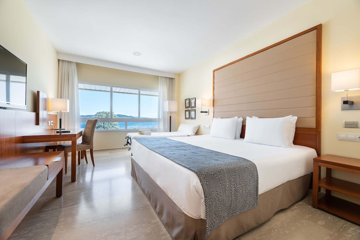 A hotel room with a large bed, a desk, a chair, and a view of the outdoors.