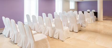 A conference room with rows of white chairs and a black table, large windows, and a purple wall.