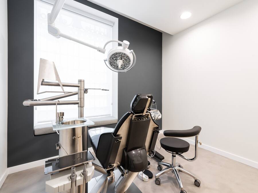 Una clínica dental moderna con un sillón de exploración amplio, una luz dental y un lavamanos.