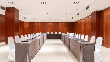 A conference room with a long table, white chairs, and a brown tablecloth.